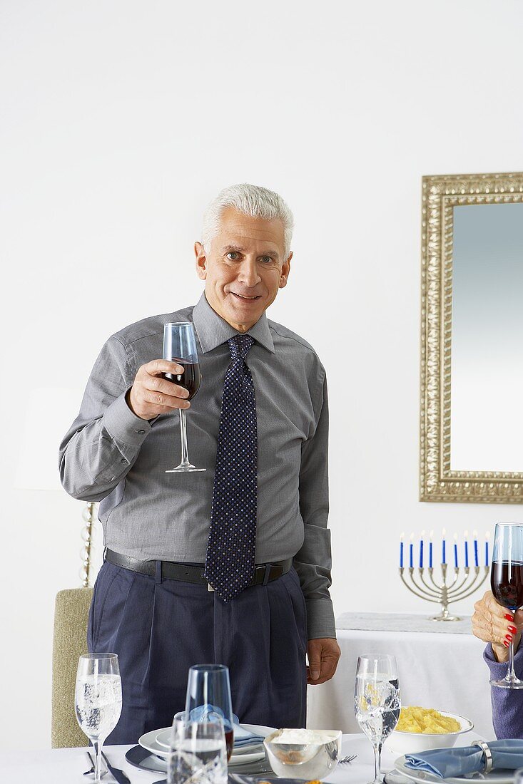 Man at Head of Hanukkah Table Holding a Glass of Red Wine