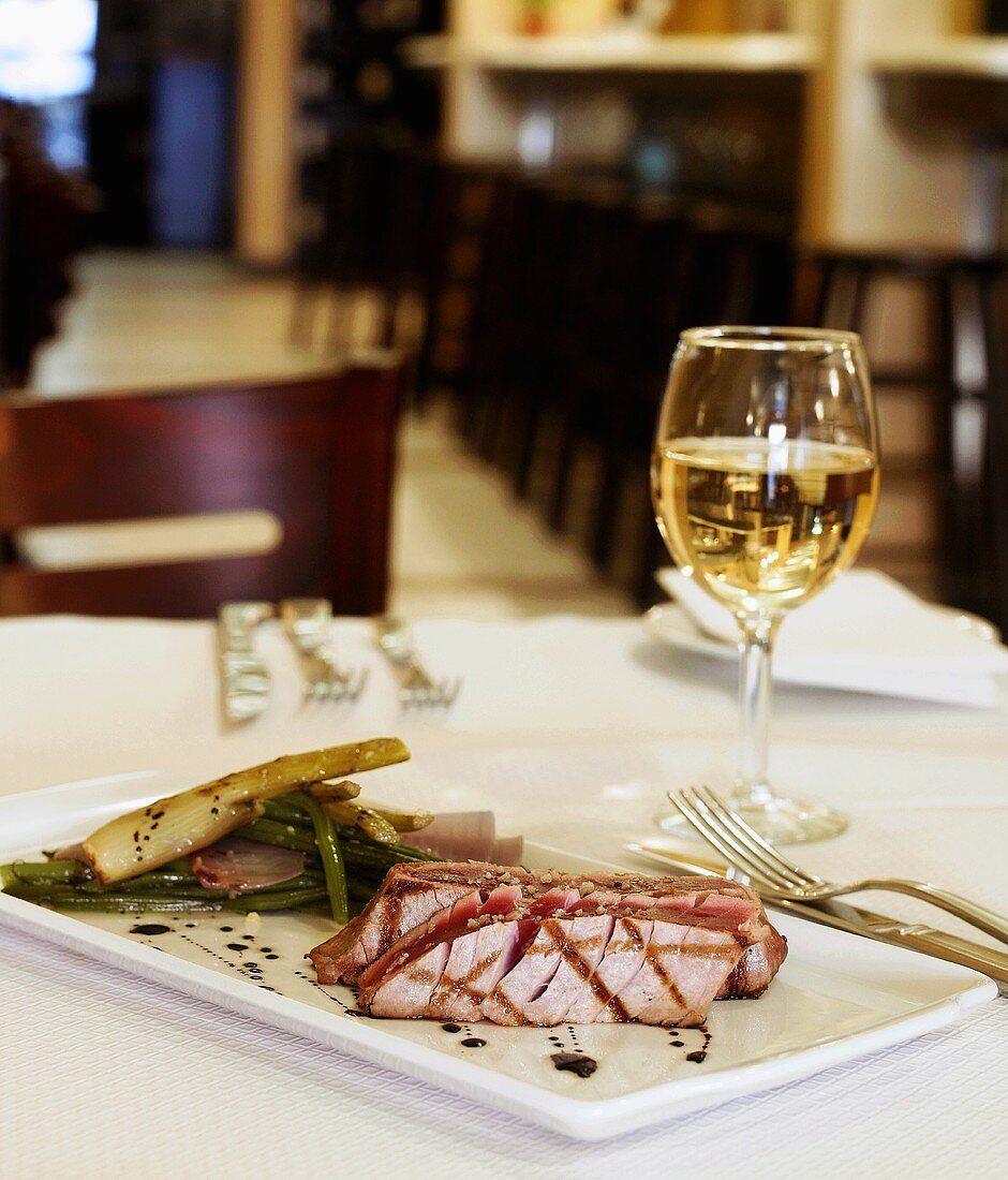 Seared Tuna with Green Beans and a Glass of White Wine on a Restaurant Table