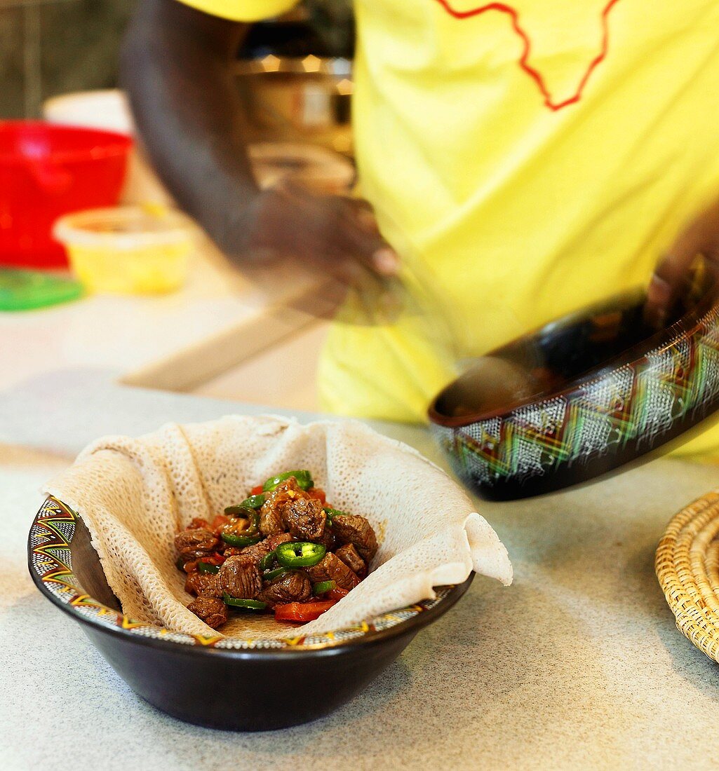 Chef Spooning Beef and Vegetable Dish onto Injera Bread in a Bowl