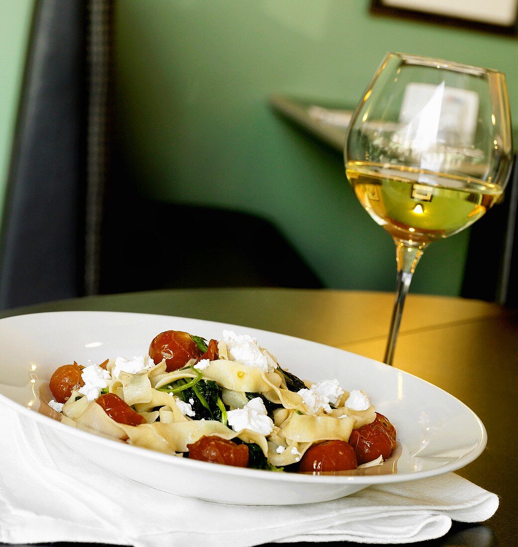 Bandnudeln mit Tomaten, Ziegenkäse und Rucola, Glas Weißwein