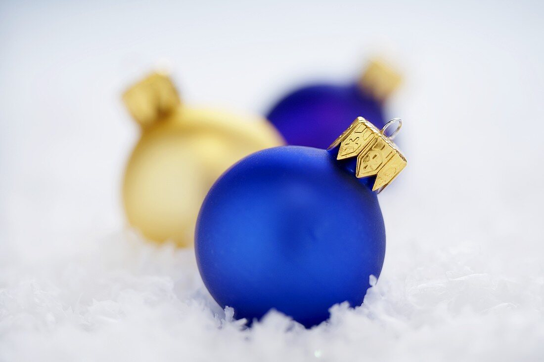 Blaue und goldfarbene Christbaumkugeln im Schnee