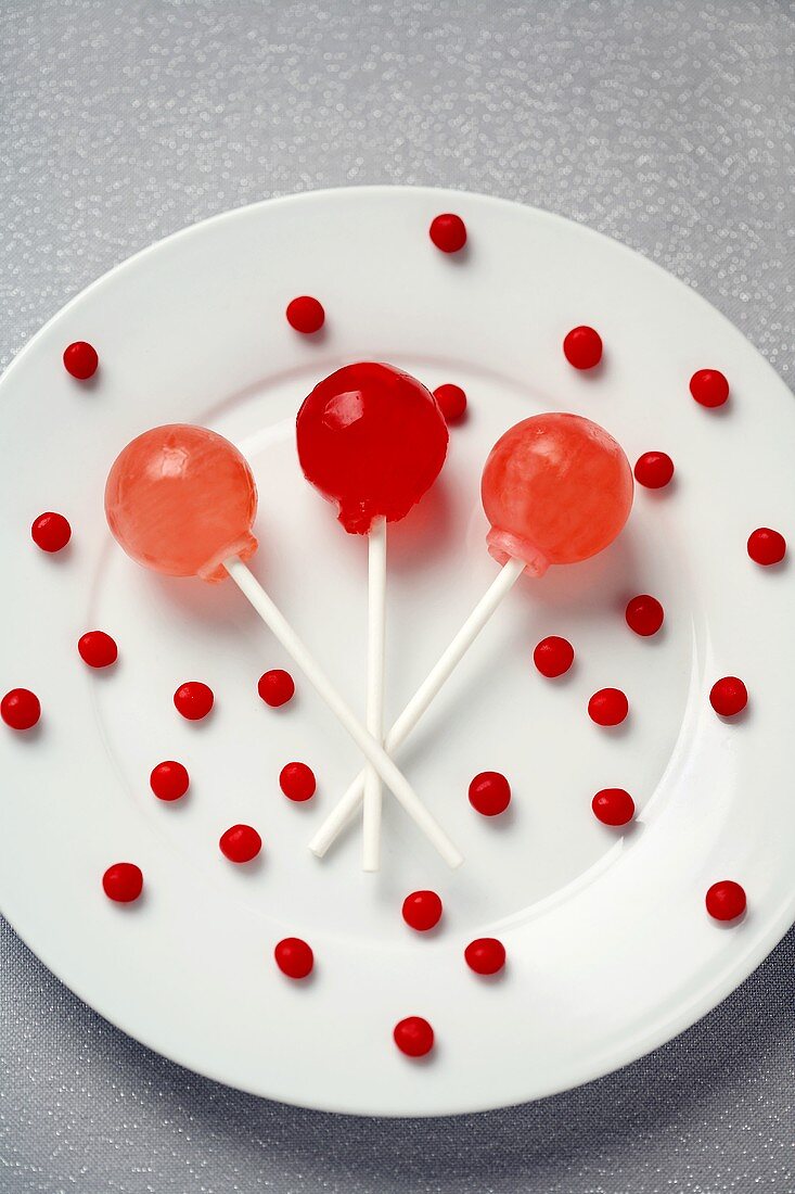 Three Lollipops with Small Red Candies on a White Plate