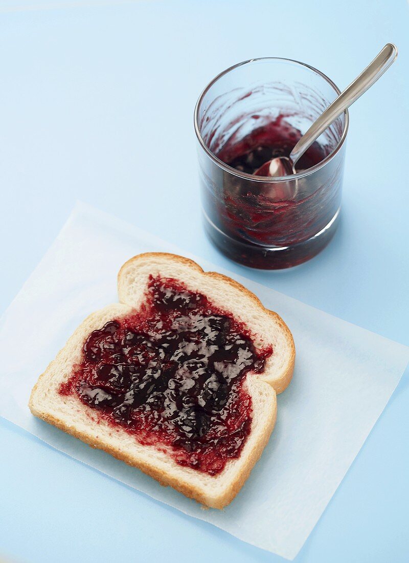 Grape Jelly Spread on a Slice of White Bread, Jelly in a Glass Cup with a Spoon