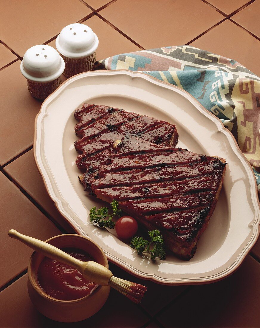 Barbecue Ribs on a Platter with a Bowl of Barbecue Sauce and Basting Brush