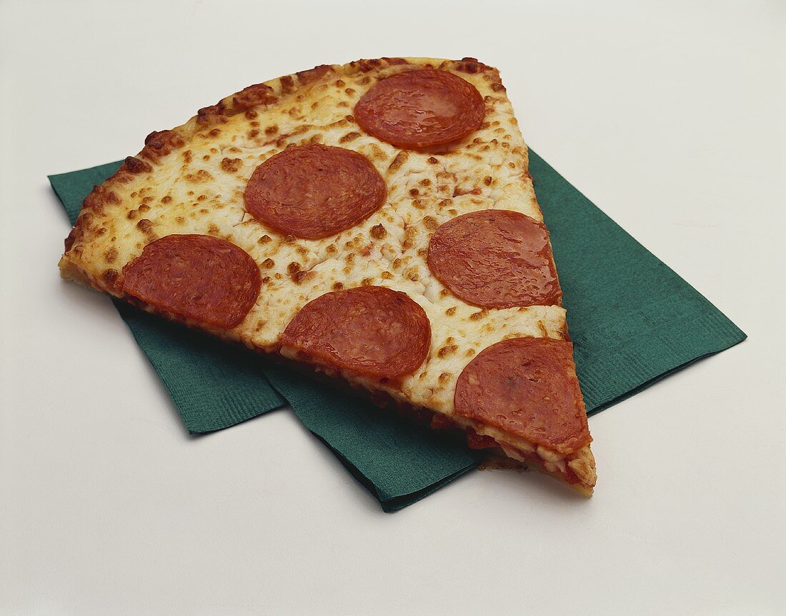 Stück Pizza mit Peperoniwurst auf grüner Serviette