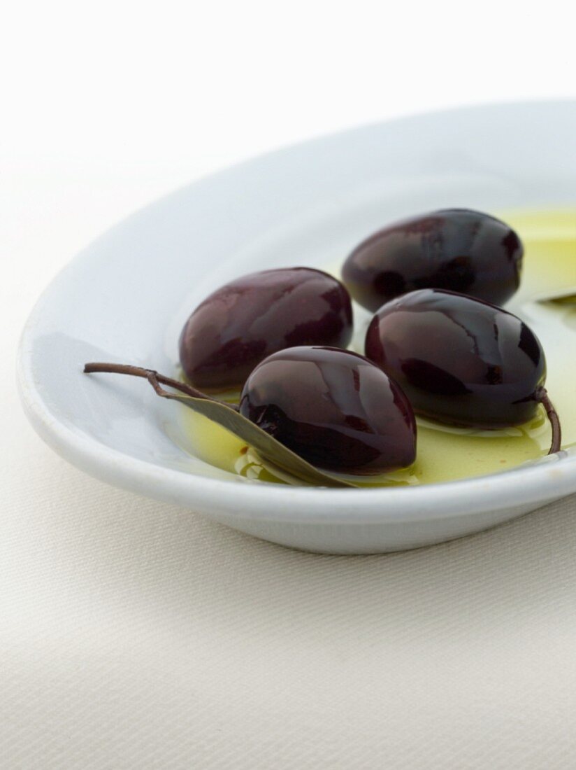 Vier Kalamata-Oliven in Schale mit Olivenöl