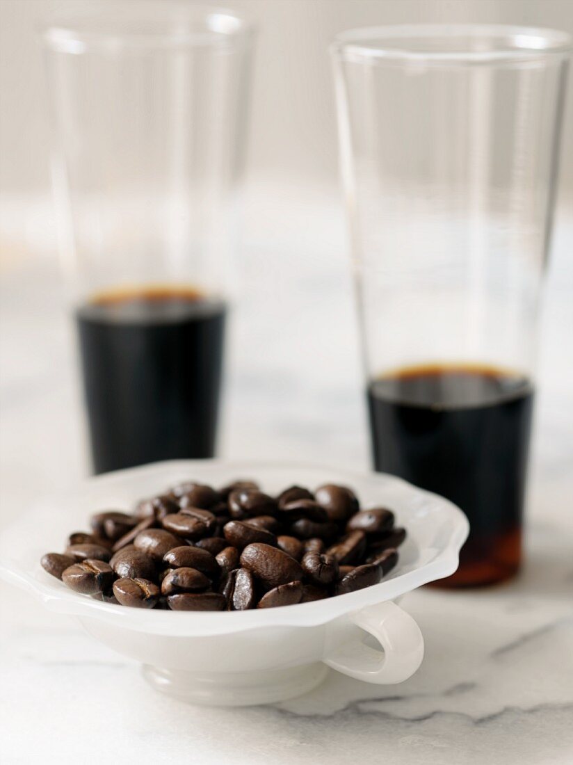 Kaffeebohnen in Schale vor zwei Gläsern Kaffee