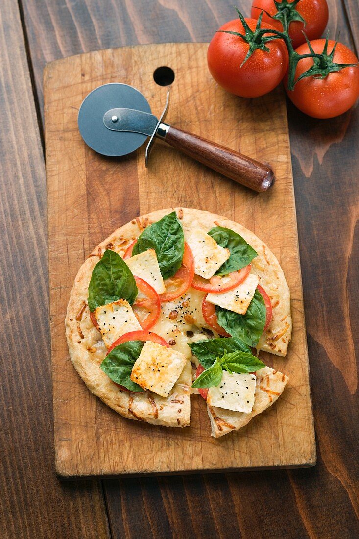 Pizza mit Käse, Tomaten und Basilikum auf Schneidebrett