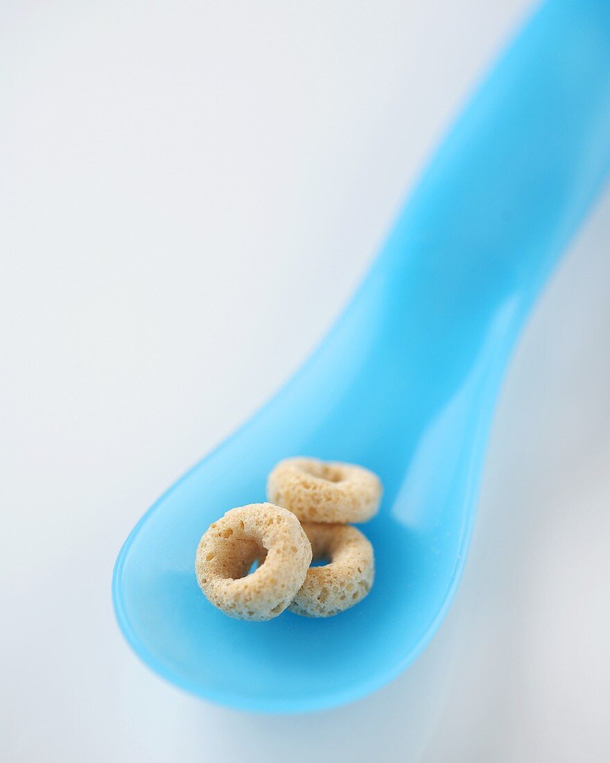 Three Pieces of Toasted Oat Cereal on a Blue Plastic Spoon