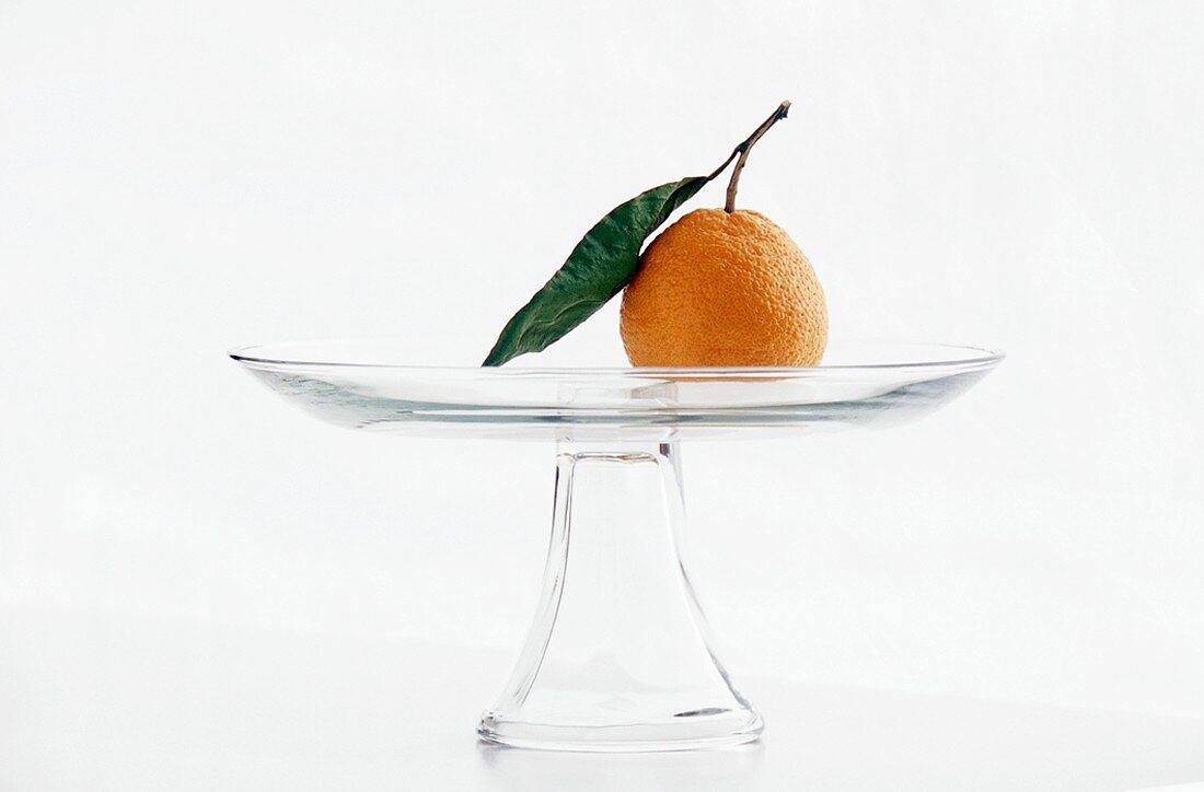Eine Tangerine mit Blatt in Glasschale