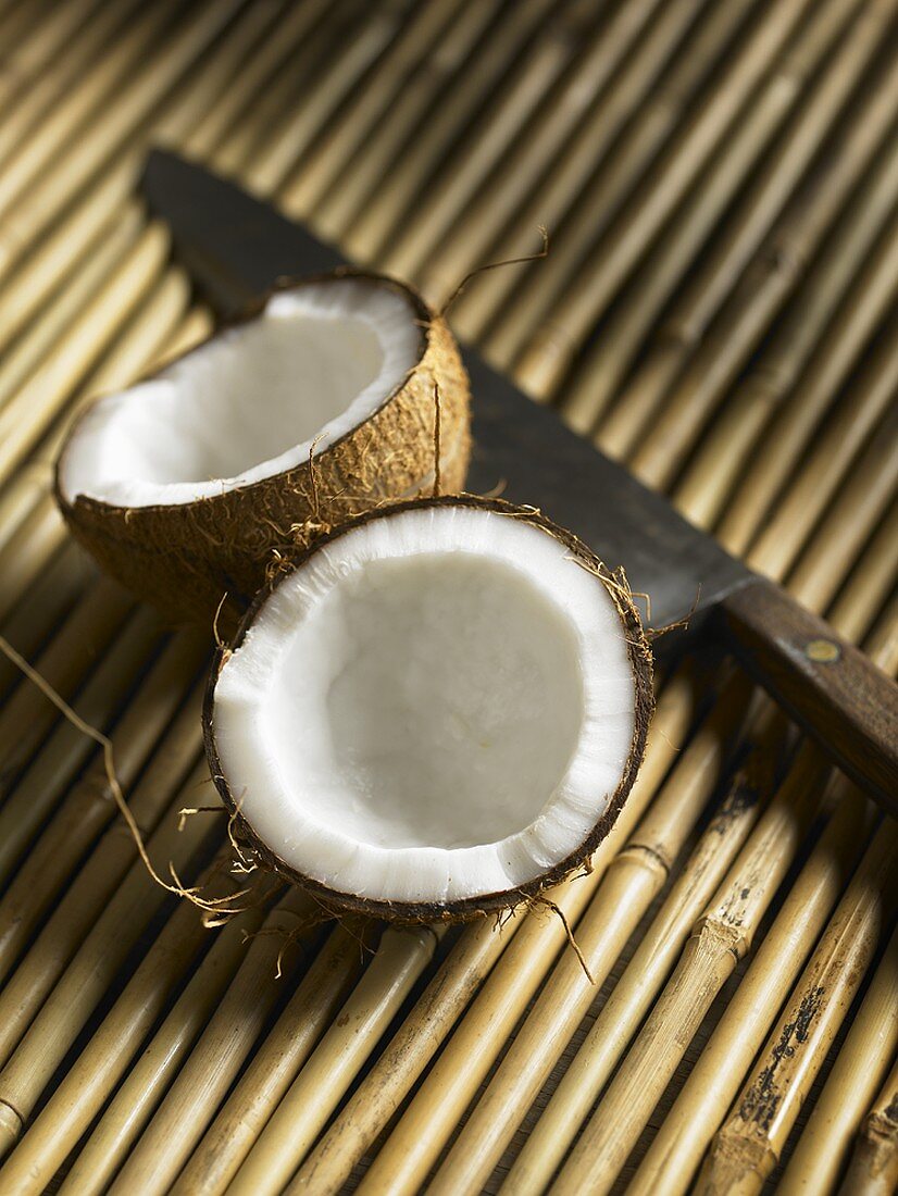 Kokosnuss, halbiert, mit Messer auf Bambus