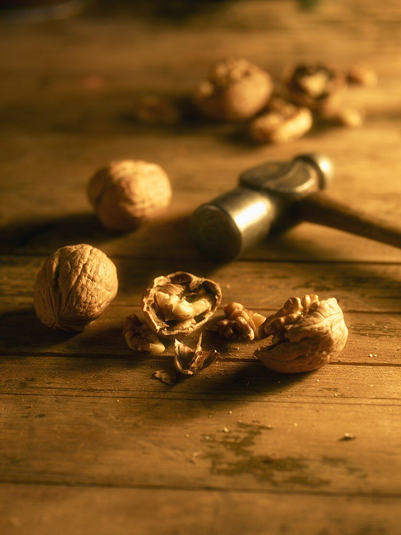 Cracked and Whole Walnuts on a Table with Small Hammer