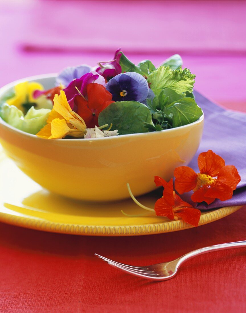 Salat mit essbaren Blüten in gelber Schale