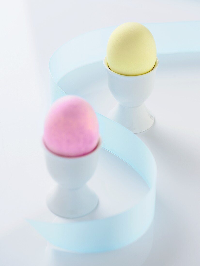 Zwei gefärbte Eier in Eierbechern, dazwischen blaue Schleife