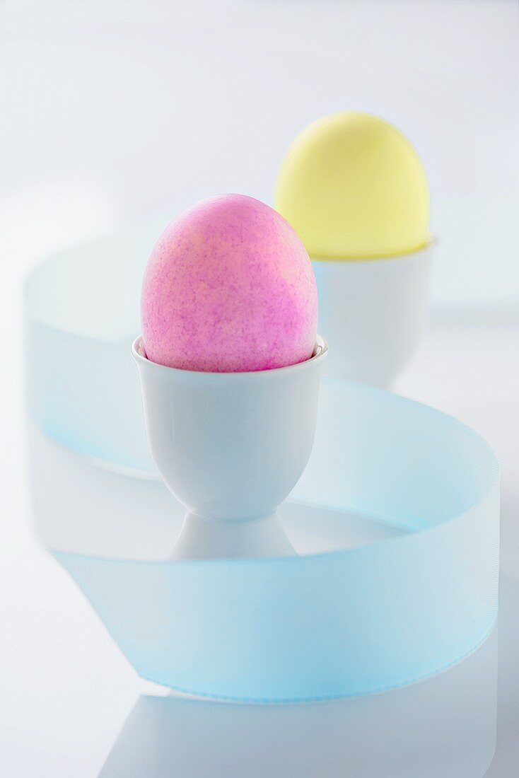 Two Colored Easter Eggs in Egg Cups, Pink and Yellow