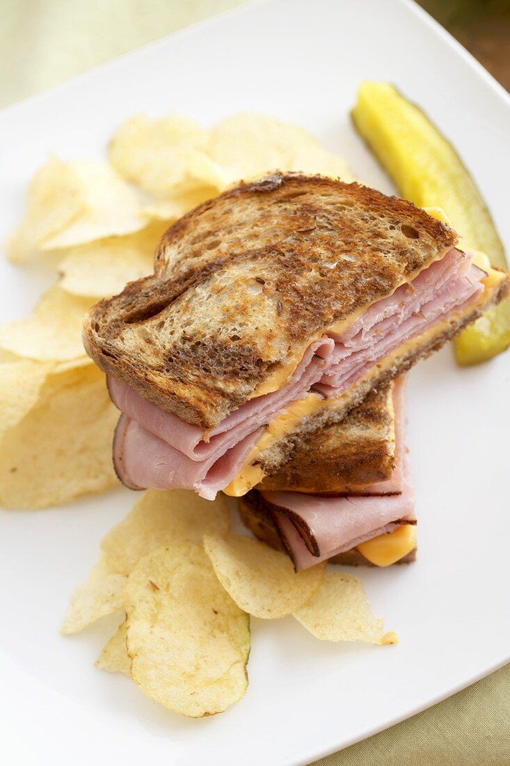 Grilled Ham and Cheese Sandwich Halved with Chips and a Pickle