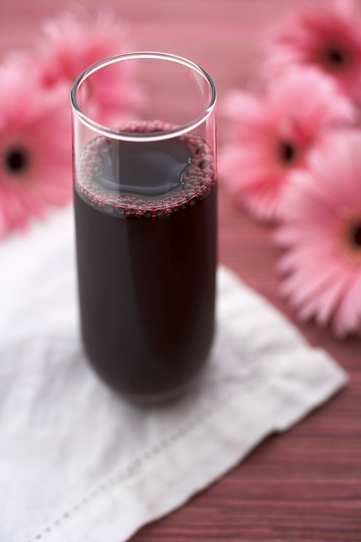 Glas Granatapfelsaft vor rosa Blumen