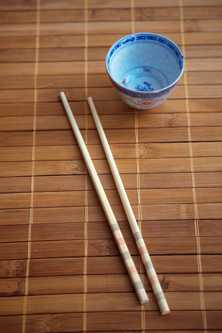 Essstäbchen und leeres Schälchen auf Bambusmatte