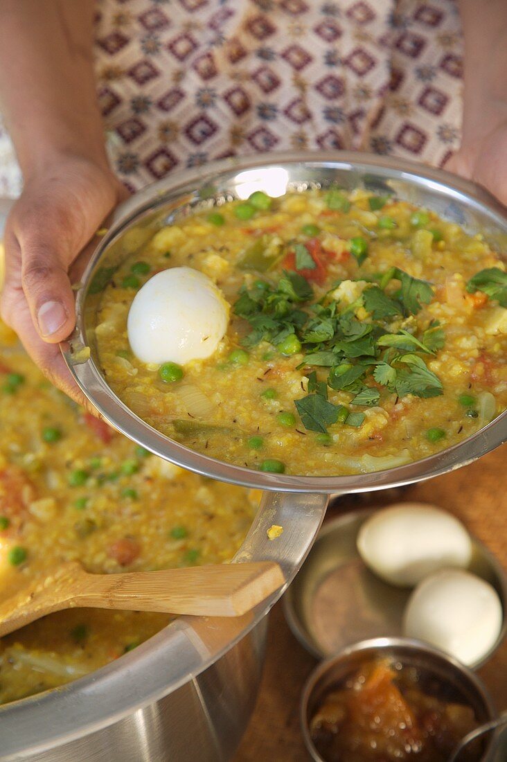Person serviert Dal mit Ei (Linsengericht, Indien)