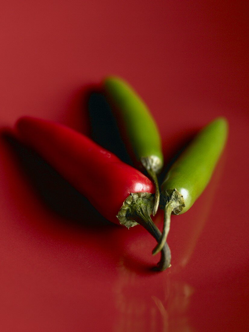 Grüne und rote Jalapeno Chilischoten auf rotem Untergrund