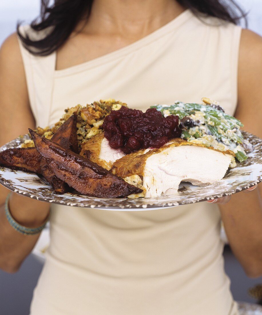 Woman holding plate of roast turkey with accompaniments
