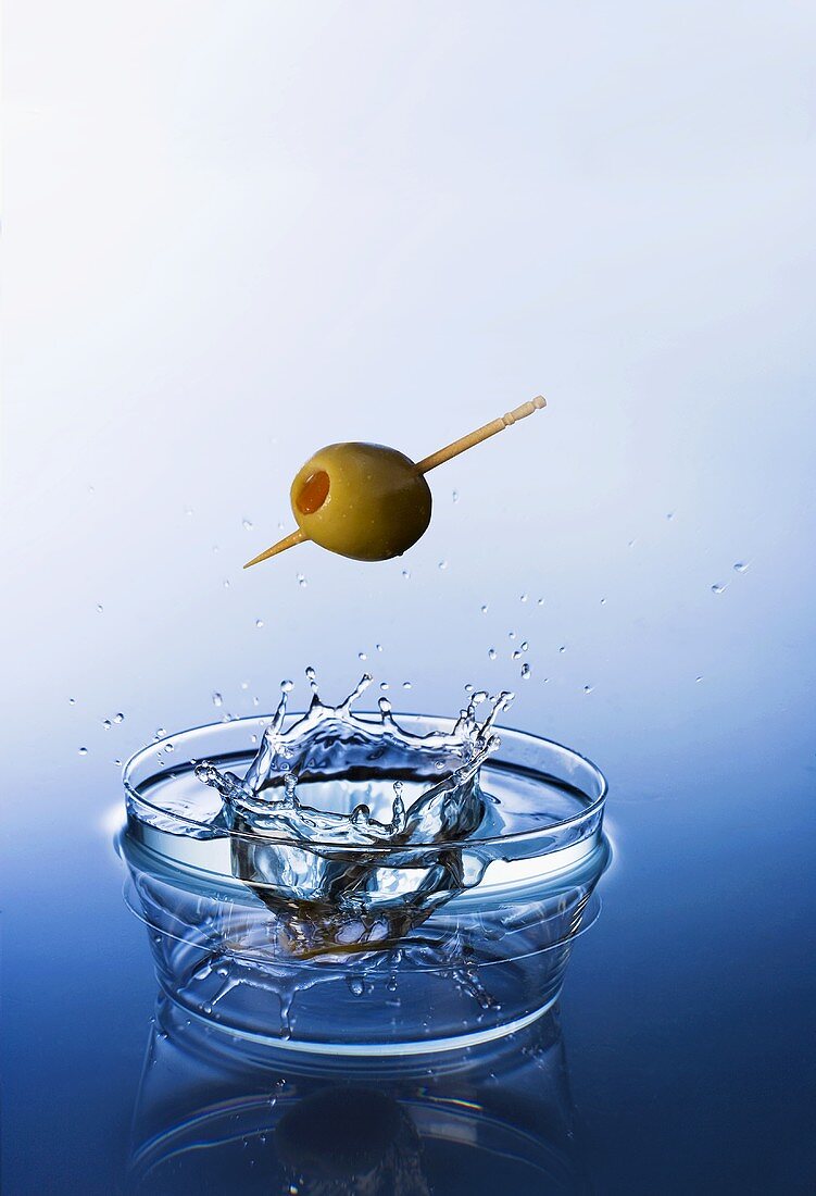 An olive with a toothpick falling into water