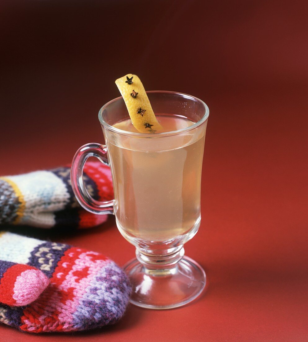 Hot Toddy Served in a Glass Mug with Lemon Rind with Cloves Garnish; Mittens