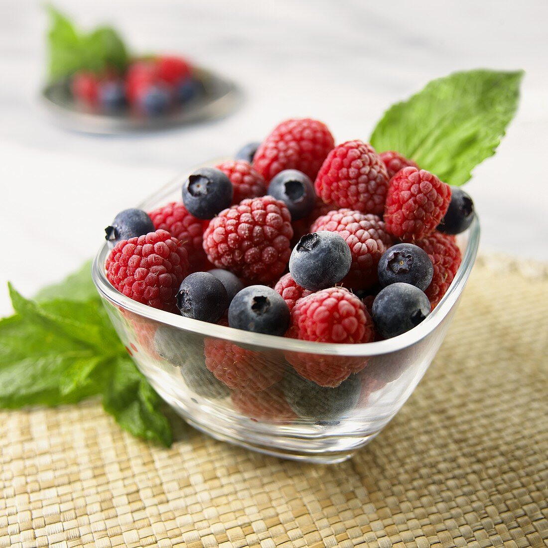 Raspberries and blueberries in glass bowl with mint
