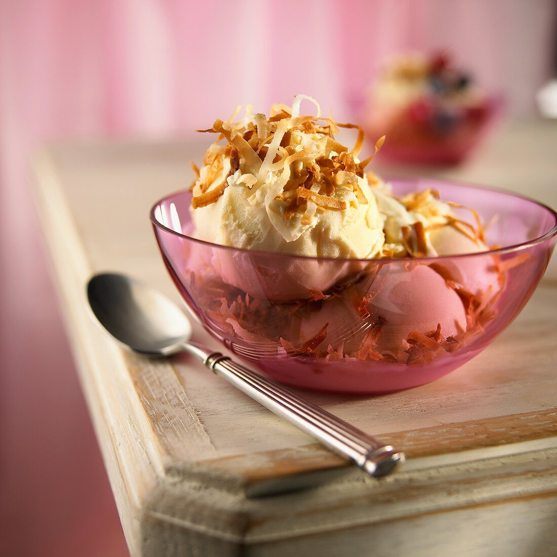 Vanilleeis mit gerösteten Kokosraspeln in rosa Glasschale