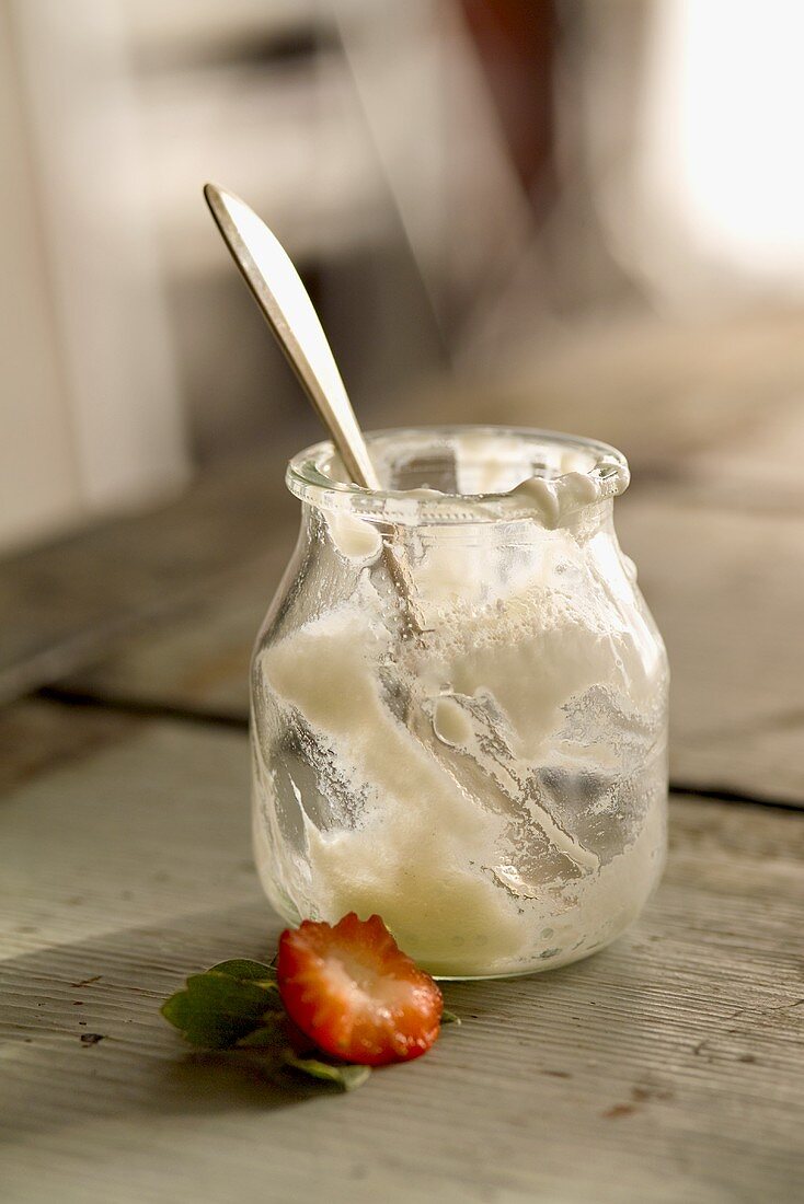 Leergegessenes Joghurtglas und Reste einer Erdbeere
