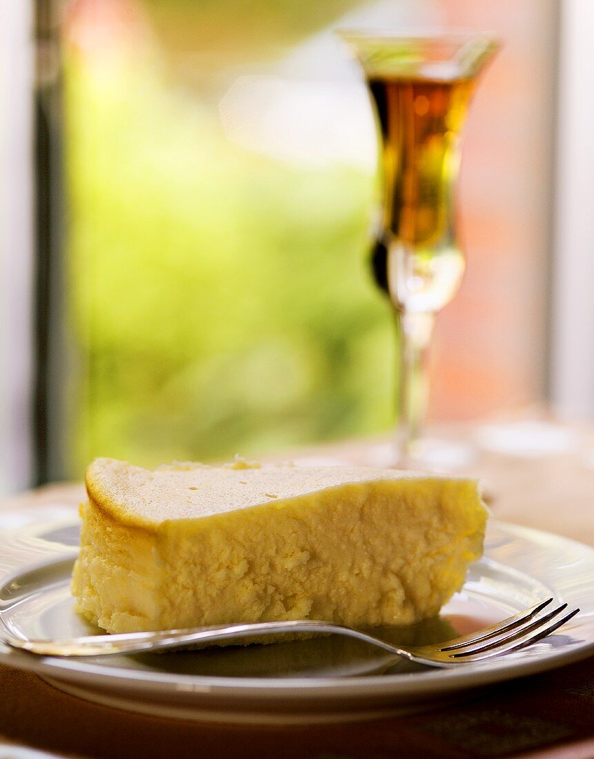 Piece of cheesecake on plate with fork; glass of dessert wine