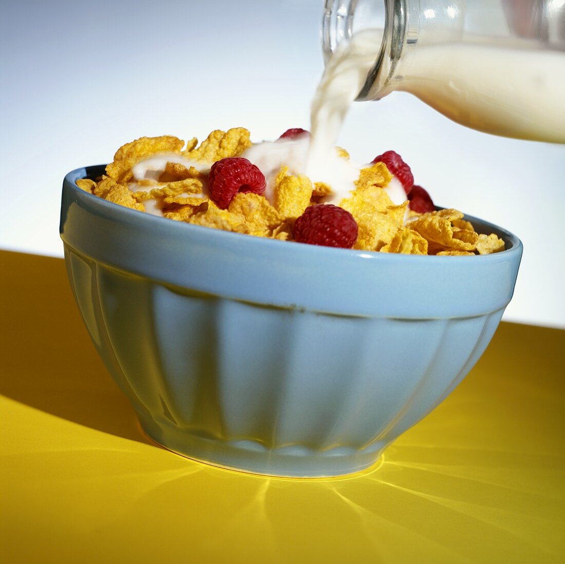 Pouring milk over cornflakes with raspberries