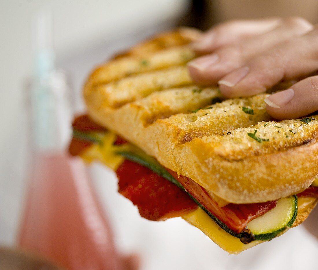 Hand hält Sandwich mit gebratenem Gemüse und Käse