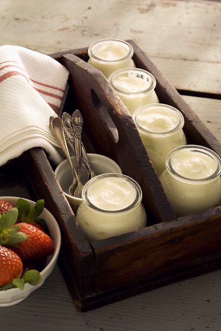 Yoghurt in jars in wooden crate; strawberries in bowl