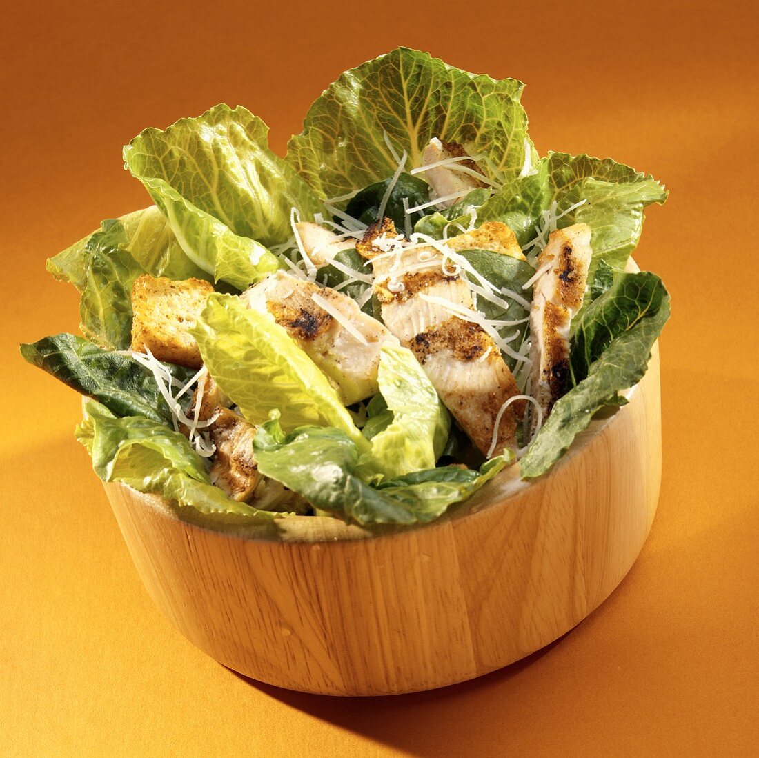 Caesar salad with chicken breast in wooden bowl