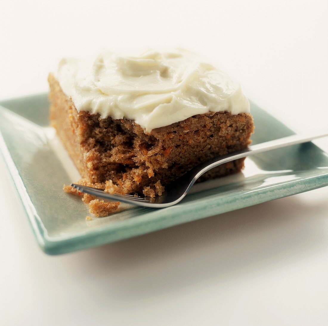 A Square Piece of Carrot Cake with Cream Cheese Frosting on a Square Green Plate with a Fork