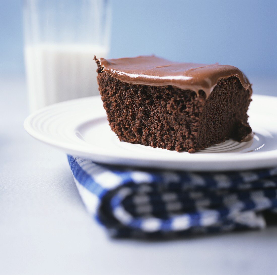 Stück Schokoladenkuchen mit Schokoglasur vor Glas Milch