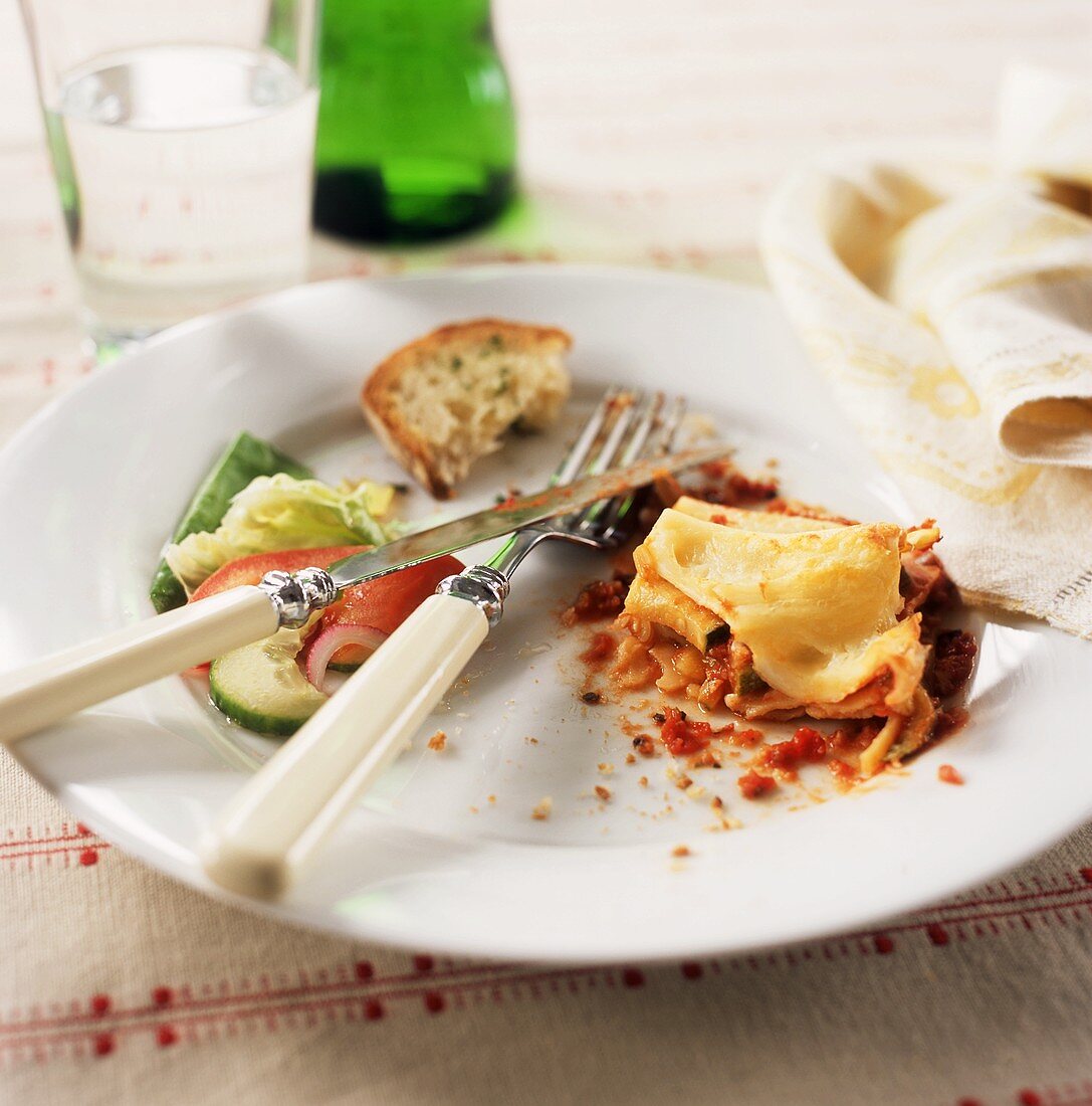 Reste von Gemüselasagne, Salat und Brot auf Teller