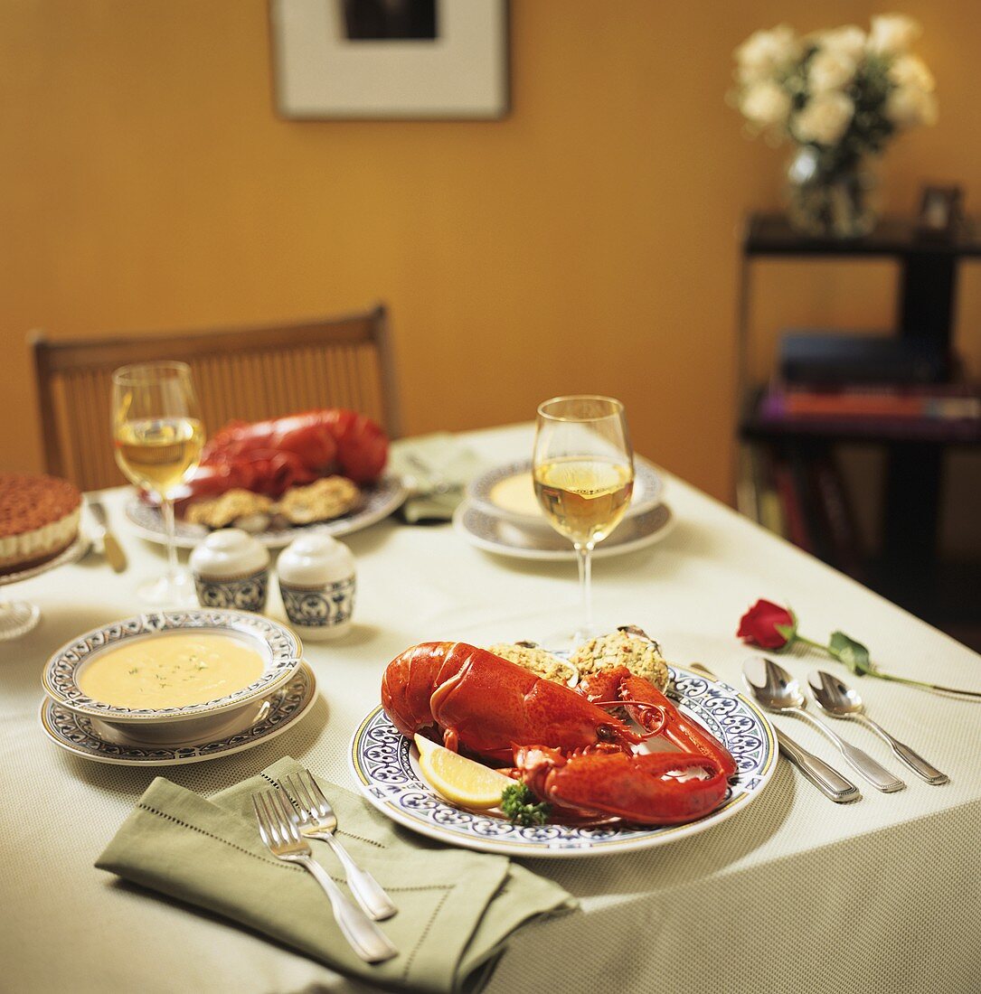 A Table Setting with Steamed Lobster, Clams Casino, Soup, Dessert and White Wine