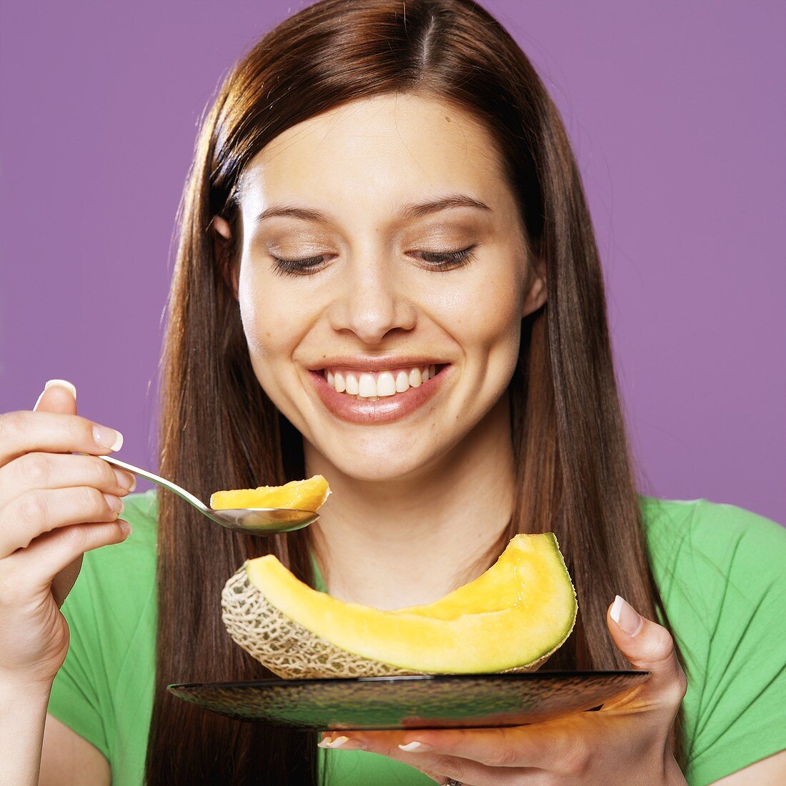 A Smiling Young Woman Taking a Spoonful of Cantaloupe