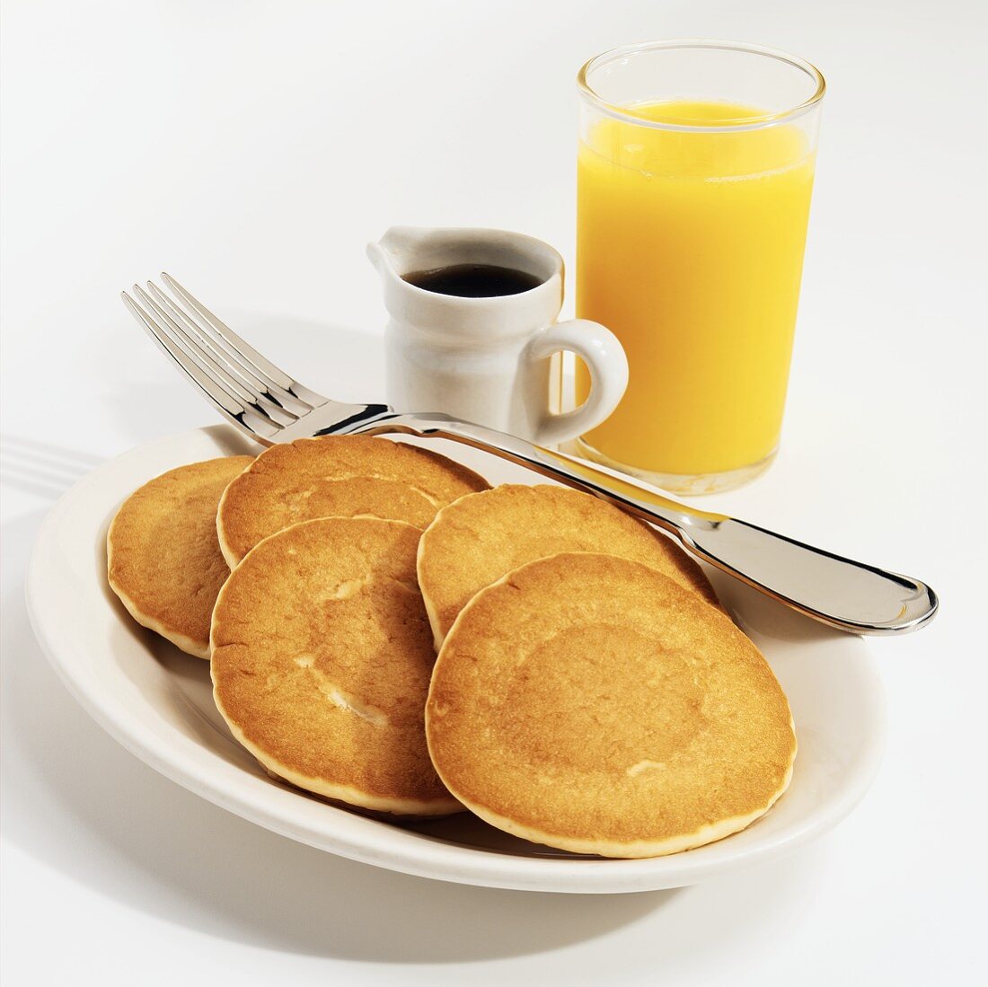 Five Pancakes on a White Plate with a Fork, a Pitcher of Maple Syrup and Orange Juice