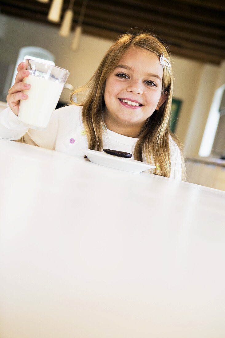 Kleines Mädchen hält Glas Milch beim Esstisch