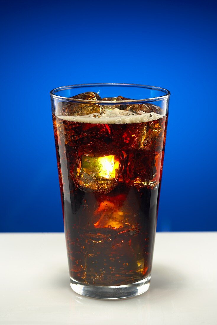 Glas Cola mit Eiswürfeln vor blauem Hintergrund