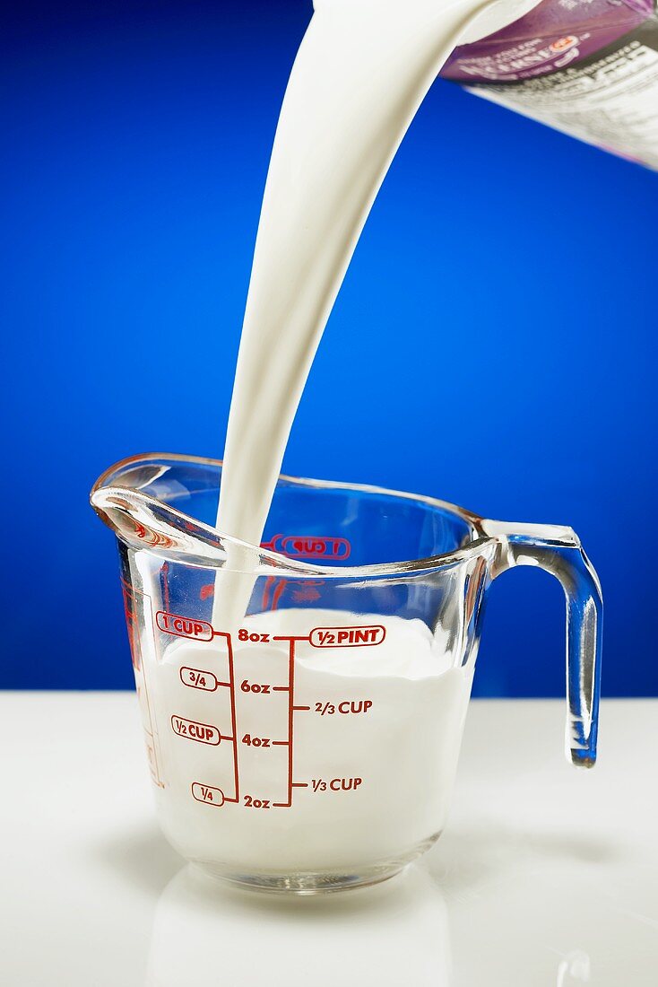 Milch in Messbecher aus Glas einschenken