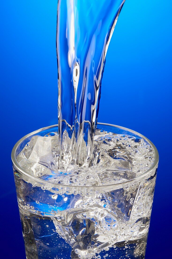 Wasser in Glas mit Eiswürfeln gießen