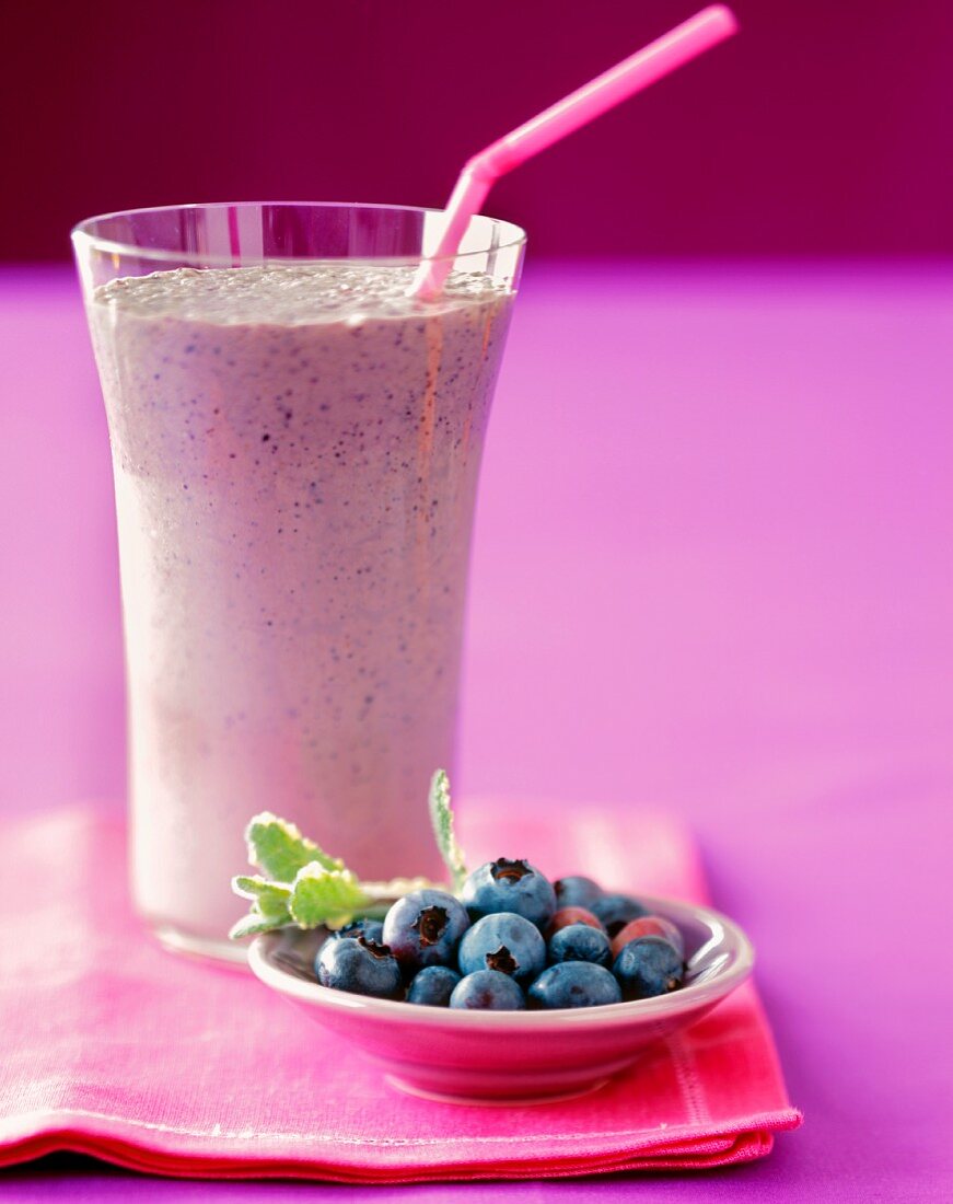 A Blueberry Smoothie in a Glass with a Bowl of Fresh Blueberries