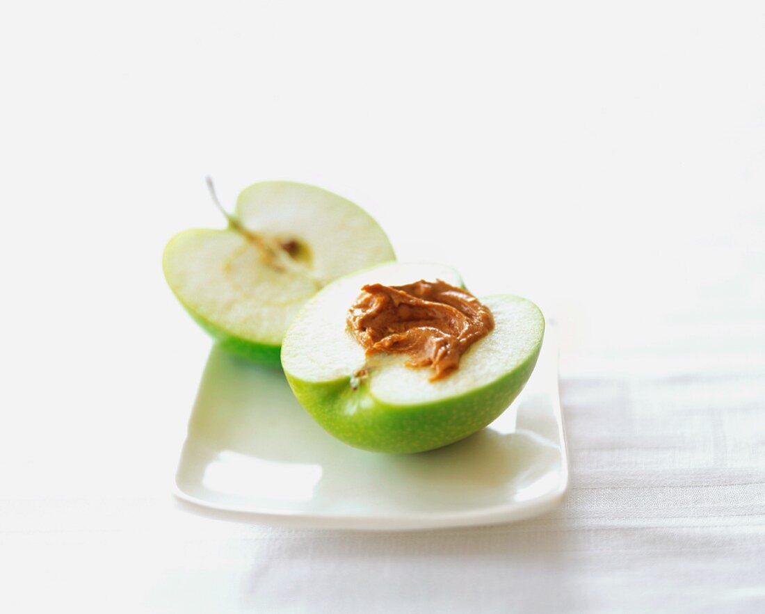 A Halved Granny Smith Apple with Almond Butter on a Square White Plate