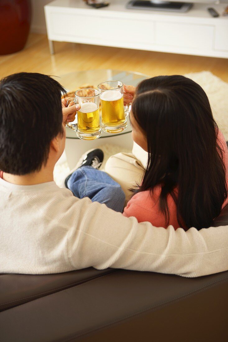Paar auf dem Sofa stösst mit Biergläsern an
