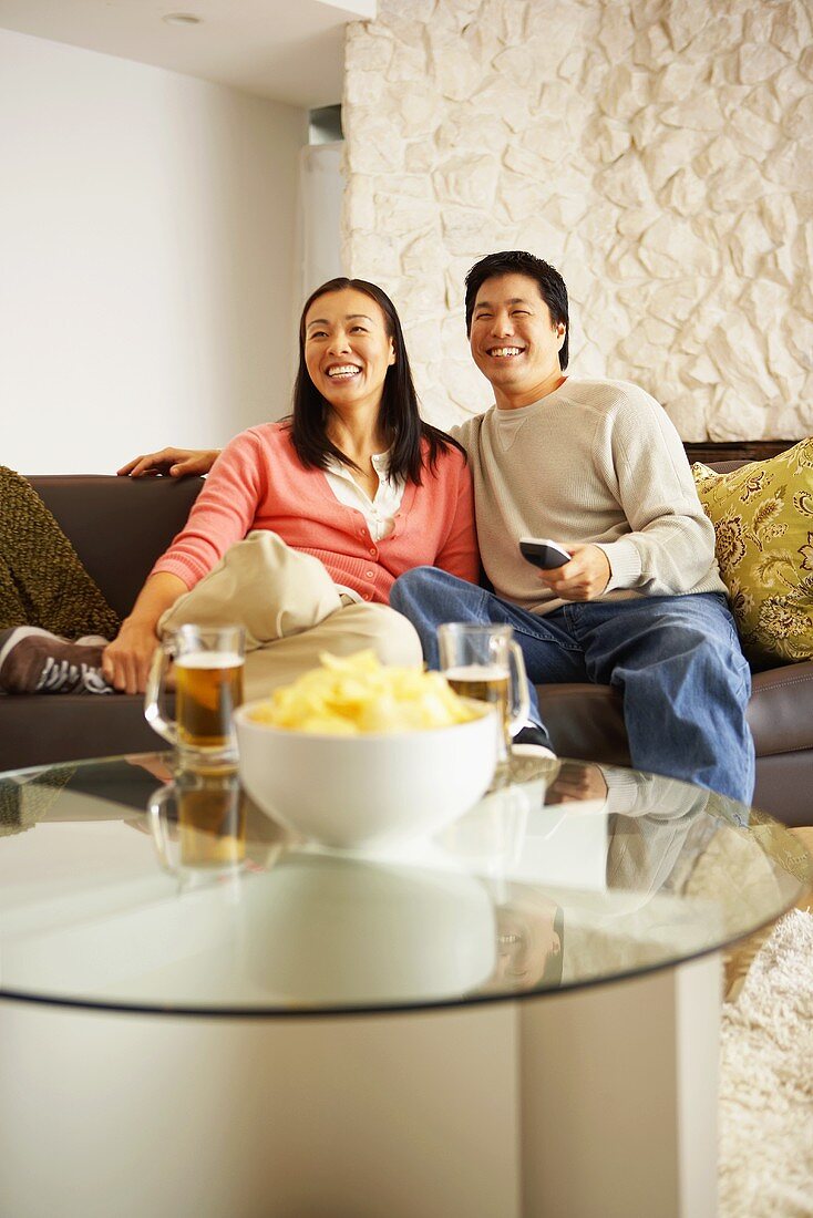 Couple on sofa watching television with crisps and beer