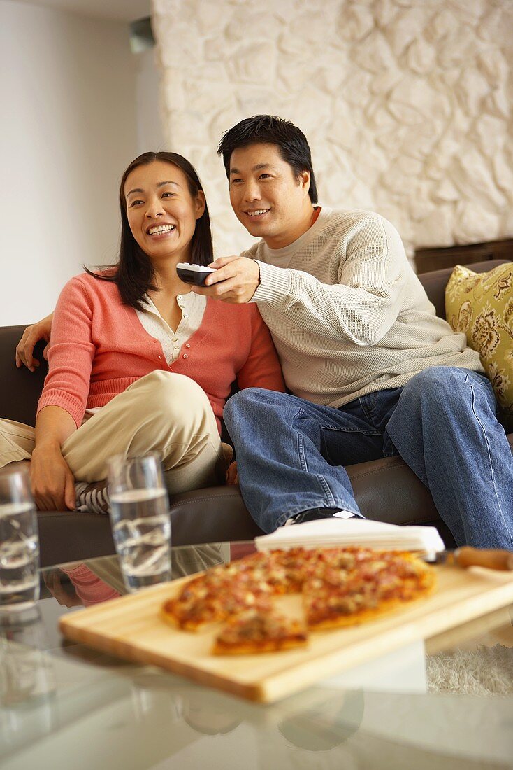 Couple on sofa watching television with pizza and drinks